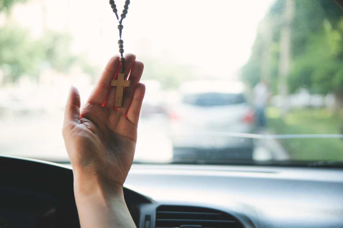 Una mano accarezza il crocifisso dentro l'auto